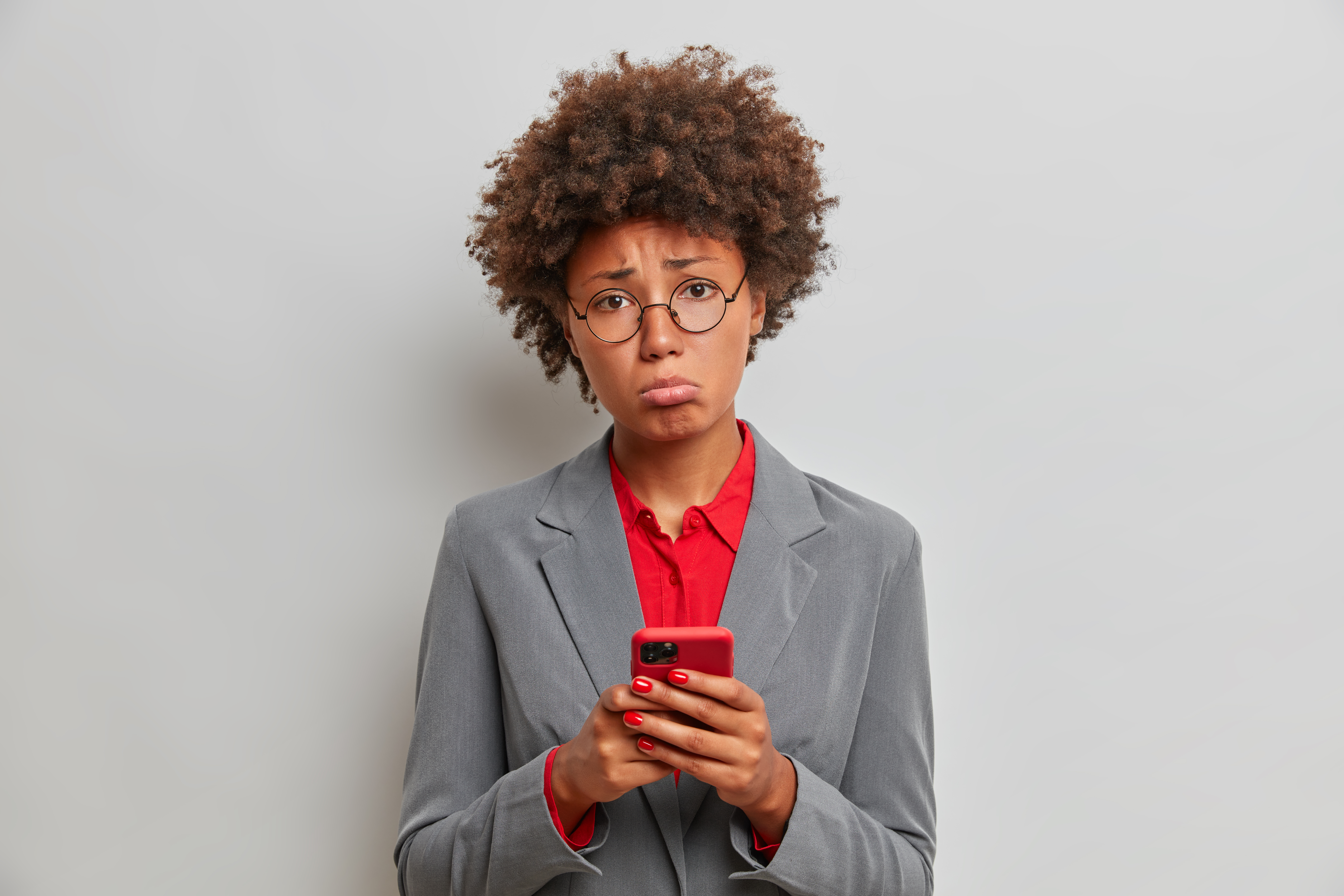 Sad disappointed female manager or executive assistant has problems at work, uses mobile phone, waits for important call, cannot solve difficult situation, stands indoor. Technology, business concept